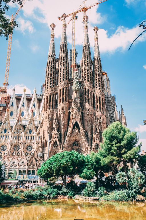 The towering spires of Sagrada Familia bathed in morning light with construction cranes visible against a blue sky